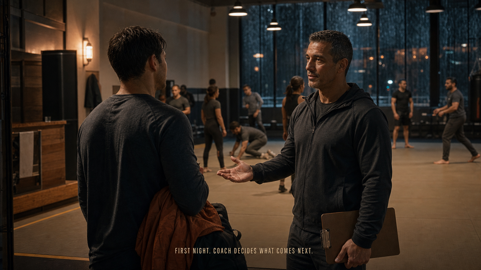 An anonymous adult beginner speaks with a coach at the edge of a warm, supervised gym while a class prepares in the background.